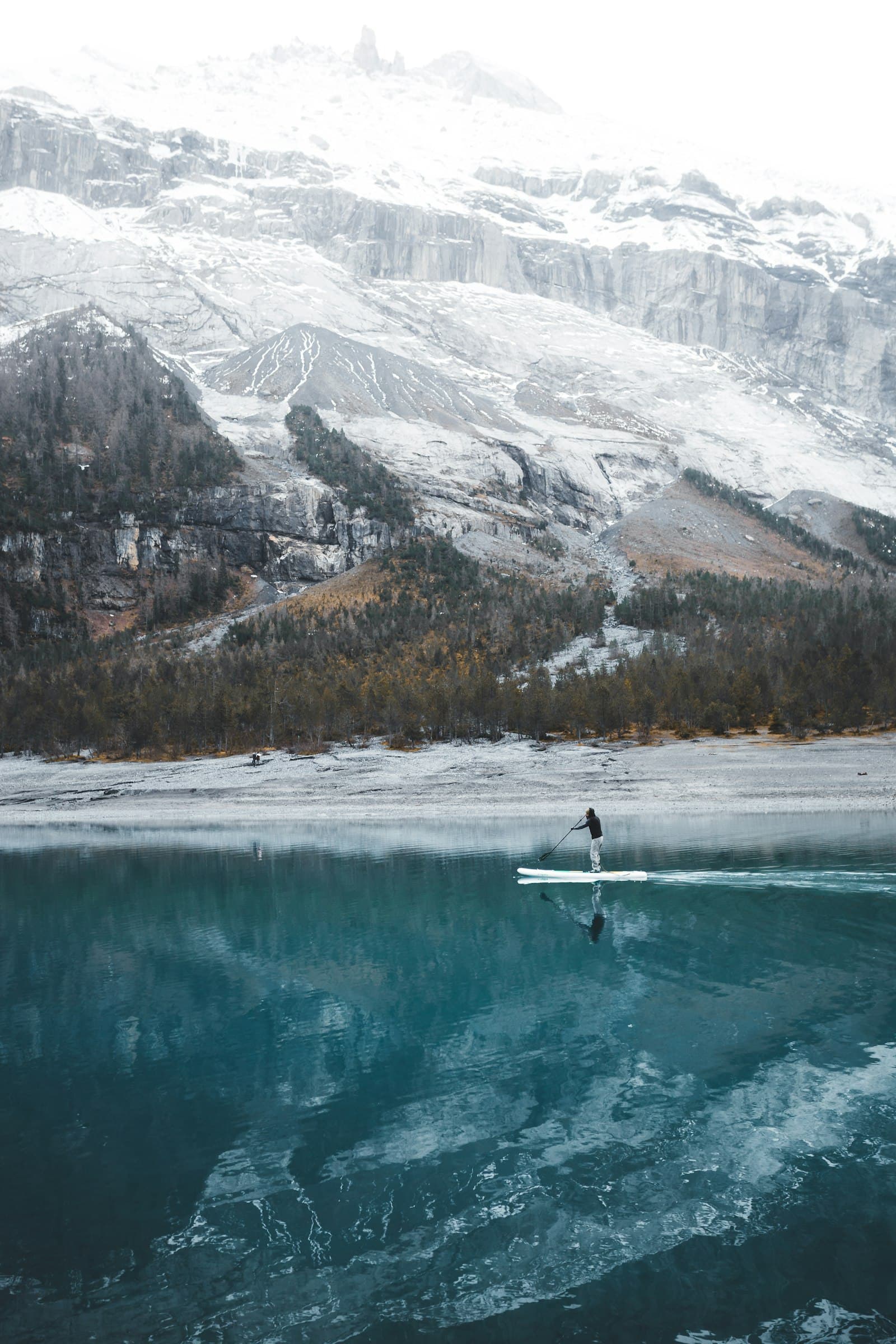 A person paddleboarding across a clear turquoise alpine lake