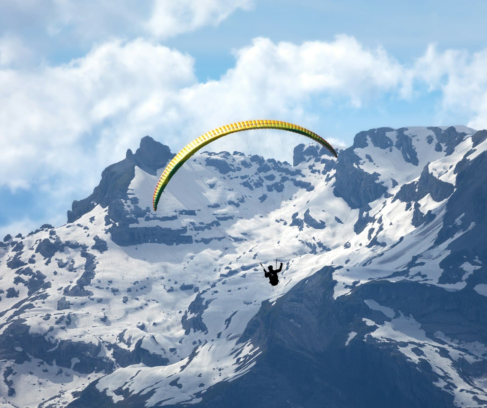 A paraglider soaring over snow-capped mountains